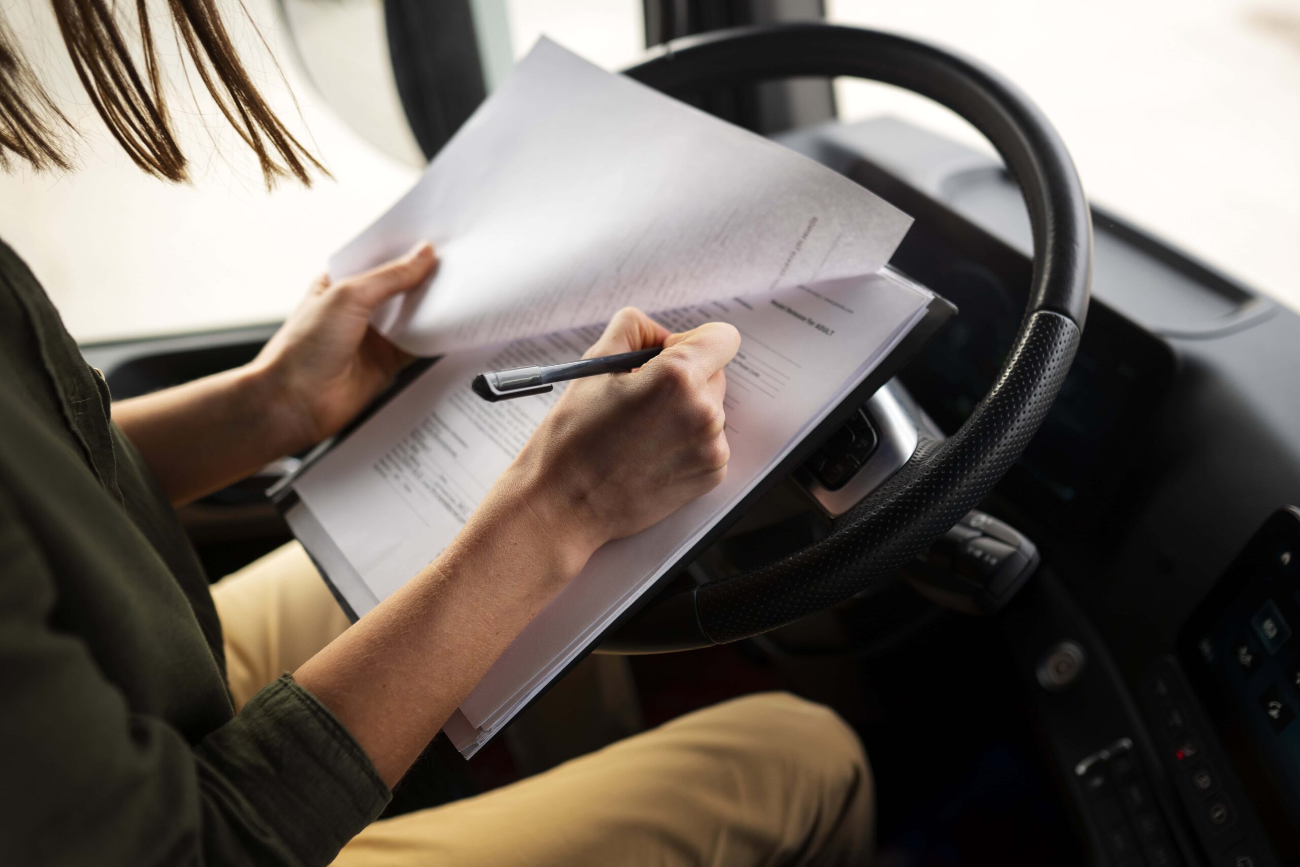 Professional female driver filling out forms inside the driver's seat of a semi truck